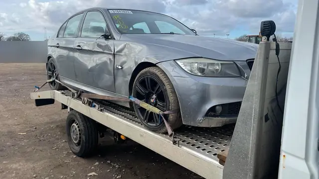 A damaged car strapped down on a recovery truck bed in daylight