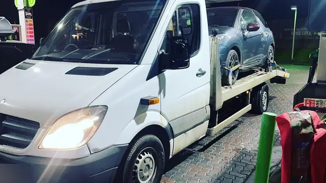 A recovery truck at a filling station at night with a car already loaded