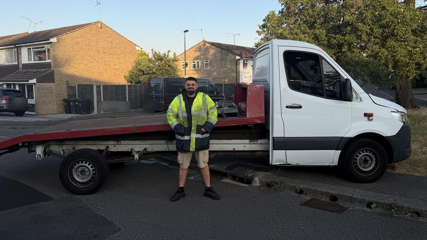 A driver beside the flatbed recovery truck, the bed tilted down to the road