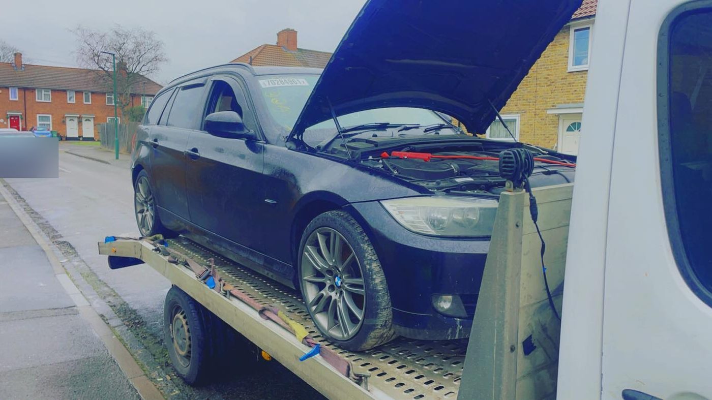 A car on a recovery truck bed with its bonnet up and jump leads on the battery
