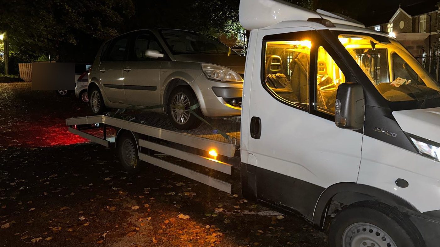 A car being loaded onto a recovery truck at night, the cab lit and the beacons on