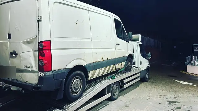 A full-size panel van loaded and strapped on a recovery truck bed at night
