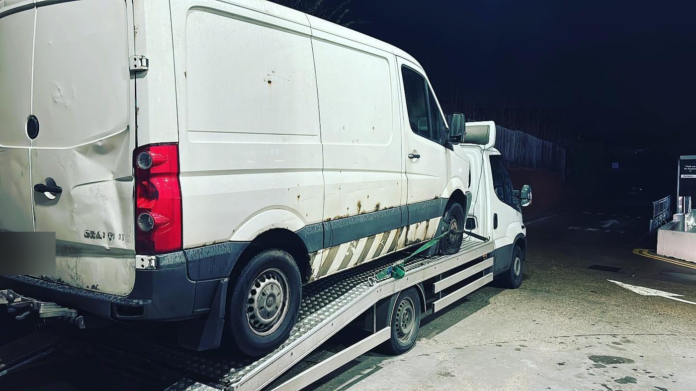 A full-size panel van loaded and strapped on a recovery truck bed at night