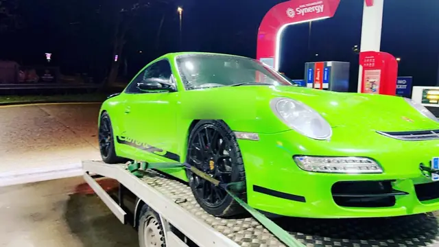 A low sports car loaded on a recovery truck bed at a filling station